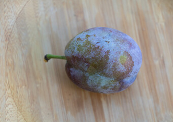 Single Ripe Plum on Wooden Bamboo Surface Close-Up