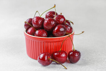 Red bowl filled with organic fresh sweet cherries with water drops on white stone surface. Seasonal...
