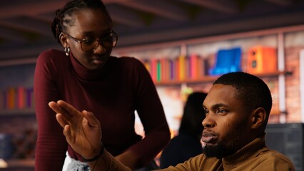 Startup cybersecurity expert in wheelchair looking for company security vulnerabilities on computer, talking with colleague. Man with disability typing on PC and chatting with coworker, camera B