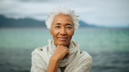 Serene elderly woman gazing at coastal horizon with tranquil sea and mountains in background