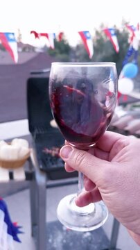 Chilean Independence Day vertical video: Man swirling wine glass in foreground with festive Chilean grill scene blurred in background