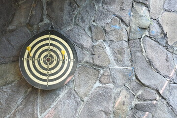 A dart board is attached to a stone wall and two yellow needles are visible 