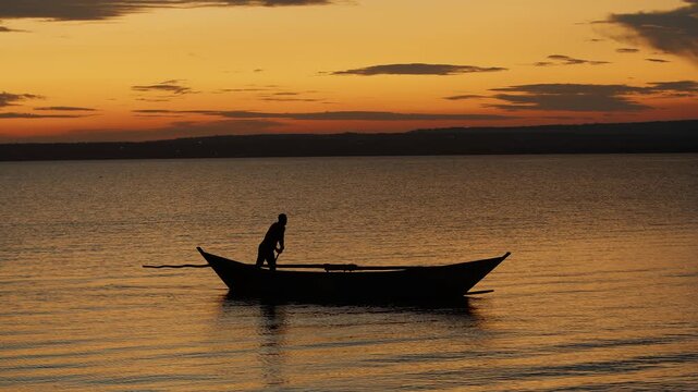 Stunning sunset on lake Victoria and african man standing in boat steers it with long pole pushing off bottom. Concept of silence and pacification