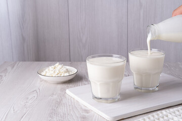 Pouring homemade kefir, buttermilk or yogurt with probiotics. Yogurt flowing from glass bottle on...