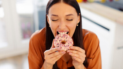 Hungry lady biting tasty doughnut, having cheat meal and eating junk food at home. Unhealthy...