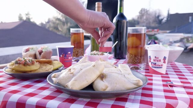 Chilean Independence Day video: Woman&rsquo;s hand serving empanadas and placing flag on food at festive Chilean table