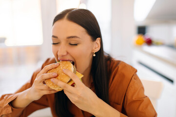 Fast food concept. Happy lady eating tasty burger, holding junk food with meat and biting, enjoying cheat meal for lunch. Unhealthy snack