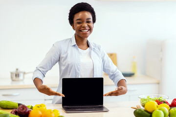 Food Blog. African Woman Showing Laptop Empty Screen Standing In Modern Kitchen At Home, Smiling To...