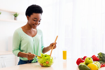 Young African American Woman Making Salad For Dinner Enjoying Meal Preparation At Home, Standing In...