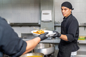 Professional cook receiving gourmet fish dish in restaurant kitchen