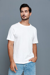 Stylish young man wearing a white t-shirt poses confidently against a solid gray background,...