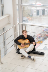 Caucasian man sitting on a staircase and playing guitar. 