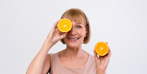 Natural fruit vitamins for mature skin. Smiling senior woman holding fresh orange in front of her...