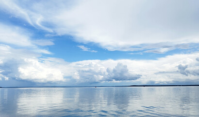 Serene water reflecting fluffy clouds, blue sky mirror image,