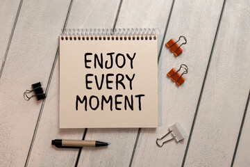 Enjoy Every Moment text with flowers frame decoration top view on blue background