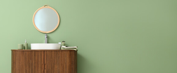 Stylish mirror hanging on green wall over sink in bathroom. Banner for design