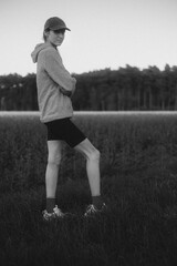 Title: A young man in a hat and hoodie, standing in the grass with folded arms, looking into the...