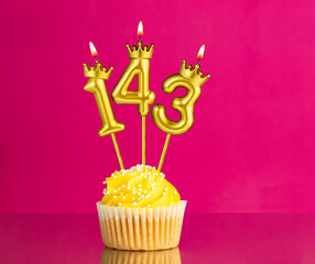 Birthday celebration with number 143 candle - Yellow cupcake on a pink background