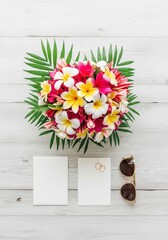 Elegant tropical flat lay mockup of weedding invitations. Honeymoon theme. Bouquet of frangipani (plumeria) flowers and palm leaves on rustic white wooden background. 