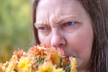 Woman making disgusted expression reacting flowering chrysanthemums, Seasonal allergies, pollen...