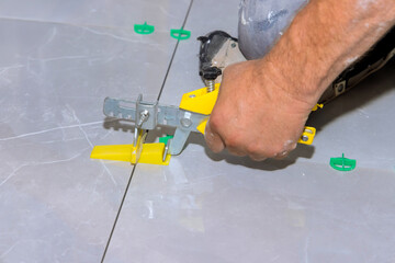 Carpenter carefully adjusts tiles using leveling tool for an even finish in home improvement...