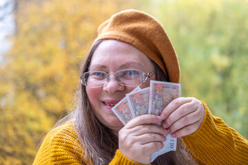 Mature white woman, 50 years old, with long hair and yellow beret presenting British GBP banknotes...