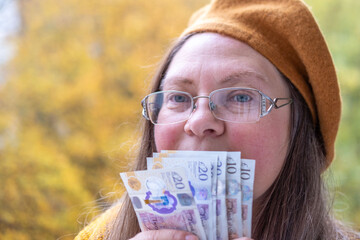 Mature white woman, 50 years old, with long hair and yellow beret presenting British GBP banknotes...
