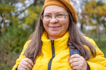 Happy middle-aged woman, Active mature tourist with backpack hiking in colorful autumn forest, nature lover, healthy lifestyle, Eco-friendly outdoor activity for older woman