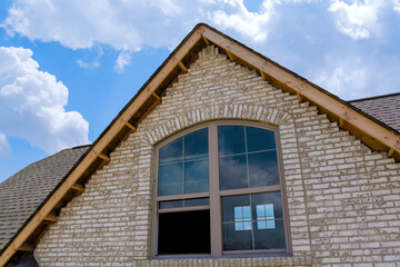Gable of brick house featuring large windows highlighting architectural details on works day.