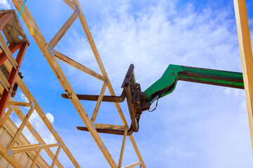 Construction site forklift telehandler lifting wooden trusses beams into place under clear blue sky.