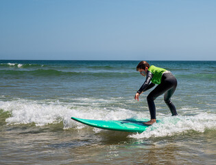 A 9-year-old boy wearing a wetsuit stands and slides on a surfboard, learning to surf in Portugal.