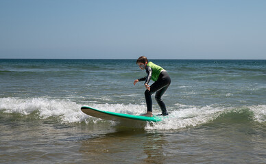 A 9-year-old boy wearing a wetsuit stands and slides on a surfboard, learning to surf in Portugal.