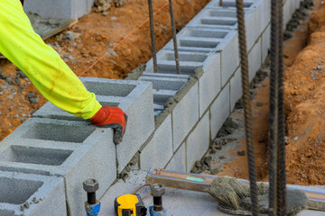 Worker carefully positions concrete blocks on foundation under construction, focusing on accuracy...