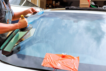 Technician uses tools to replace cracked windshield at car repair facility during work day.