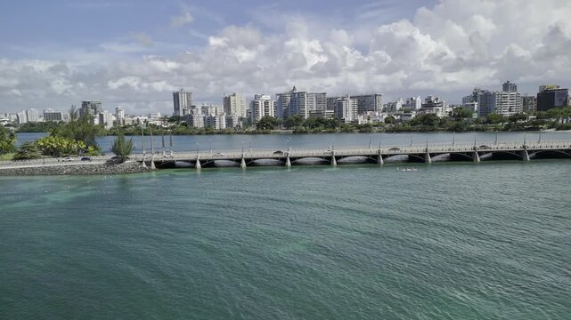 Drone flies backwards from the causeway crossing the Laguna del Condado toward seaside fort on sunny morning in San Juan, Puerto Rico