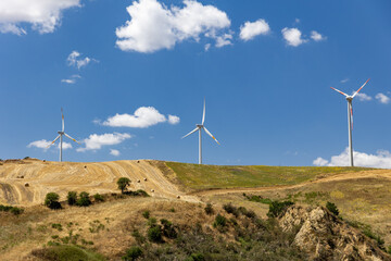 Italy. Apulia. Wind turbines on hills with fields and trees.