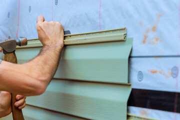 Contractor worker carefully attaches facade PVC siding to house, on precision craftsmanship in...