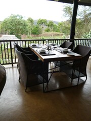 Breakfast table elegantly arranged on wooden veranda, featuring panoramic views of verdant African wilderness during peaceful morning light
