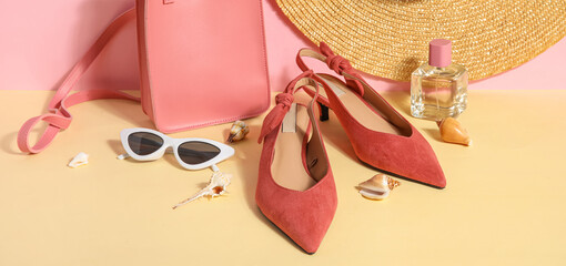 Pair of high heeled sandals with sunglasses, bag and wicker hat near pink wall