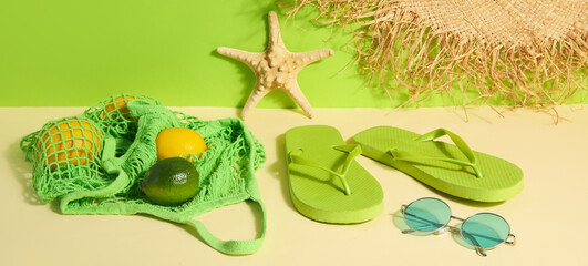 Flip flops with bag, sunglasses and wicker hat near green wall