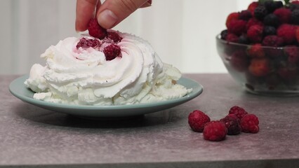 Meringues mini pavlova cakes with whipped cream decorated with fresh raspberries and blueberries berries and mint leaves on white marble background. Light summer dessert.