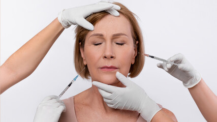 Injection cosmetology for skin rejuvenation. Beauticians making anti-aging shots into mature...