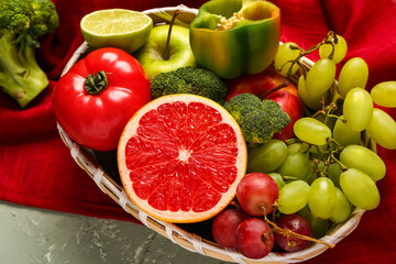 Wicker bowl with different fresh fruits and vegetables on grey background, closeup