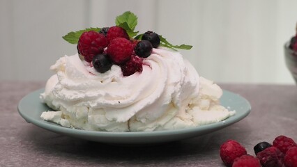 Meringues mini pavlova cakes with whipped cream decorated with fresh raspberries and blueberries berries and mint leaves on white marble background. Light summer dessert.