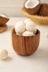 Wooden bowl with tasty coconut candies on white table