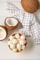 Bowl with white chocolate candies and coconuts on light wooden table
