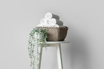 Wicker basket with towels and plant on table near light wall