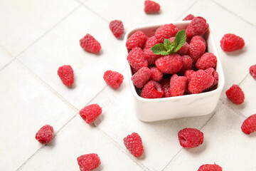 Bowl with fresh raspberry and mint on light tile background, closeup