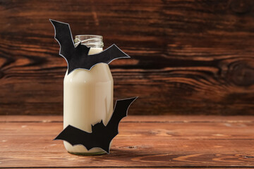 Bottle of milk and bats made of paper for Halloween on wooden background, closeup