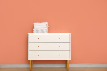 Stack of clean towels on chest of drawers near color wall